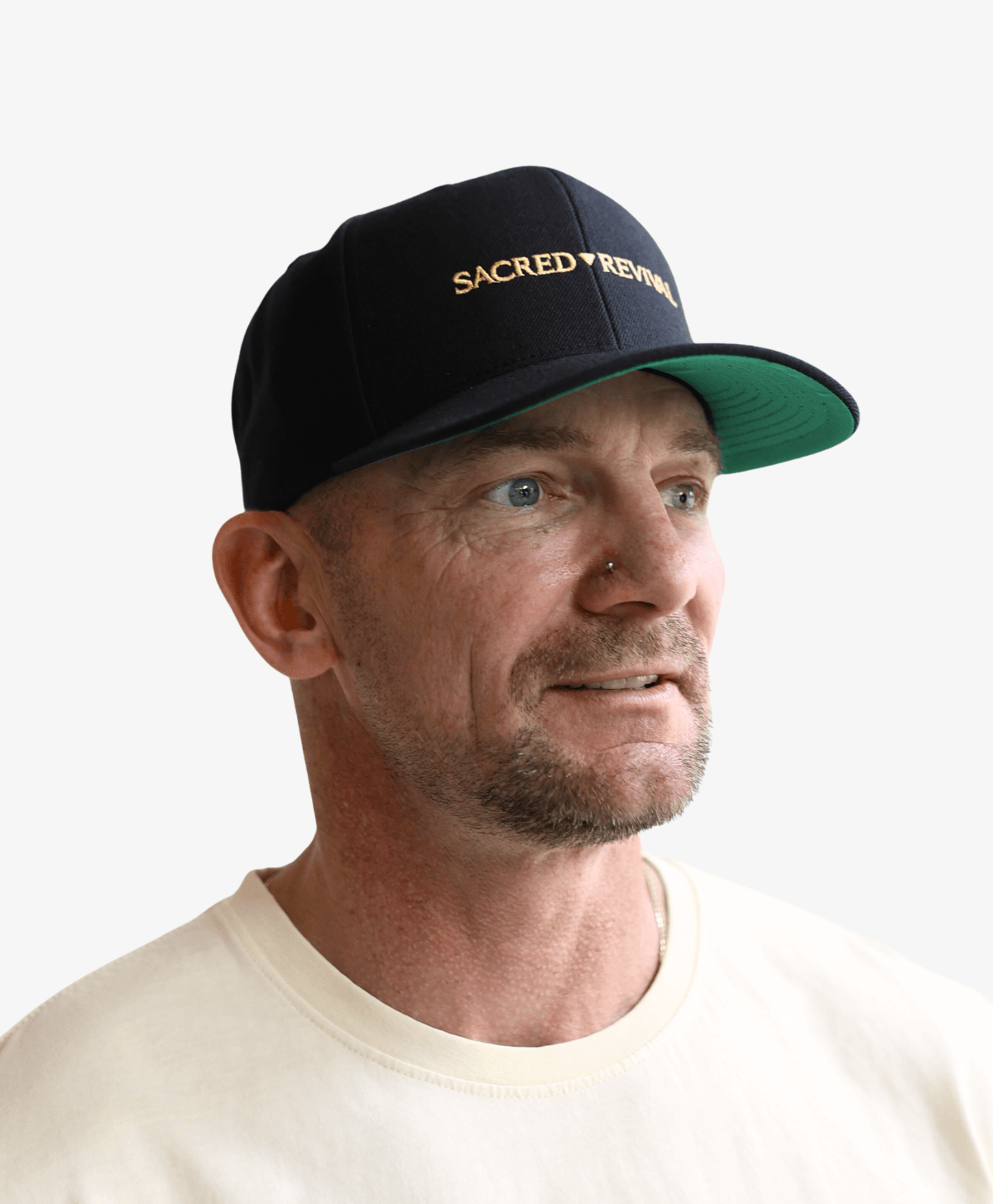 Man wearing the black Sacred Revival snapback cap with the gold wordmark, looking to the side