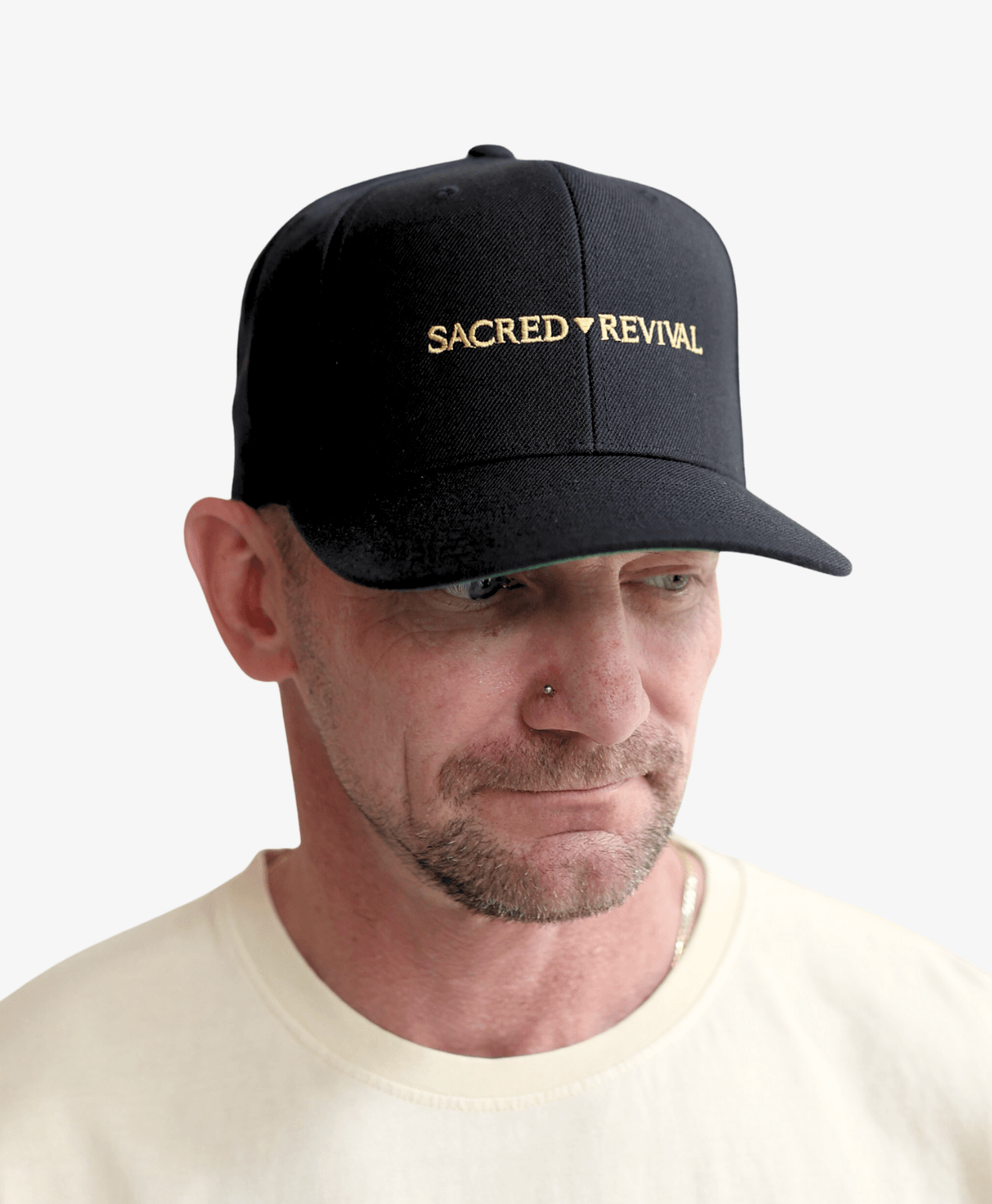Man wearing the black Sacred Revival snapback cap with the gold wordmark, side view