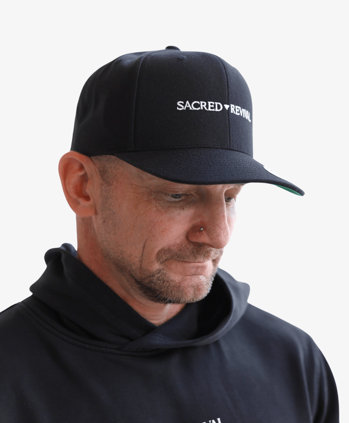 Man wearing the black Sacred Revival snapback cap, looking down