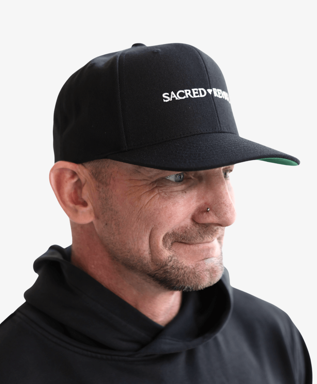 Man wearing the black Sacred Revival snapback cap with the white wordmark, side view